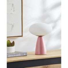 a pink and white lamp sitting on top of a wooden table next to a plant