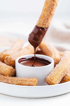 chocolate dipping sauce being poured onto some sugared donuts on a white platter