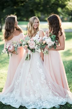 three bridesmaids in pink dresses holding bouquets and looking at each other with smiles on their faces