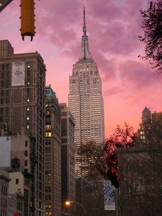 the sky is pink and purple in new york city at dusk, with skyscrapers lit up