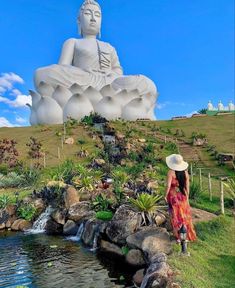 a woman standing next to a body of water in front of a large buddha statue