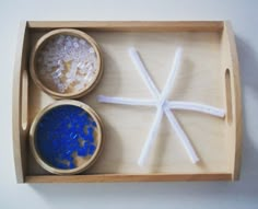 two bowls with rice and salt sit in a wooden tray on top of a table