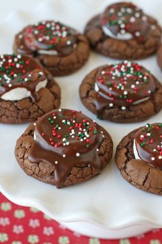 chocolate cookies with white and red sprinkles are on a plate next to a spoon