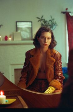 a woman sitting at a table with a candle in her hand and wearing a fur coat