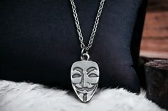 a black pillow with a silver mask on it's side and a chain around the neck