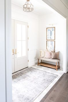 a living room with white walls and wood flooring, a bench in front of the door