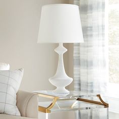 a white lamp sitting on top of a glass table next to a couch in a living room