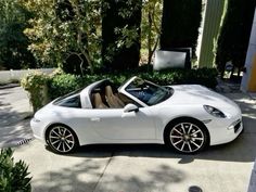 a white sports car is parked in front of some bushes and trees on the street