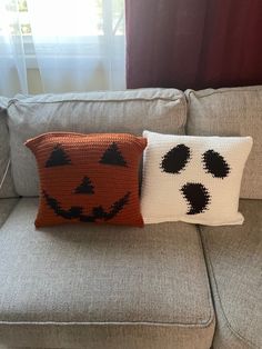 two knitted pumpkin pillows sitting on top of a gray couch next to each other