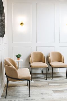 two chairs and a table in a room with white paneling on the wall behind them