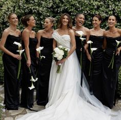 a group of women standing next to each other wearing black dresses and holding bouquets