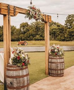 two wooden barrels with flowers and greenery on them are set up for an outdoor ceremony