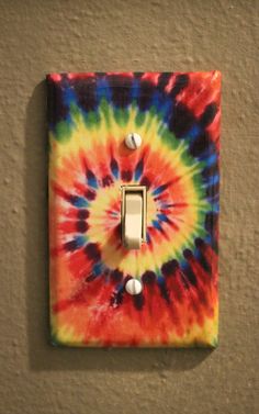 a tie - dyed light switch plate is mounted on the wall with a single outlet