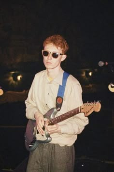 a young man wearing sunglasses and holding an electric guitar in front of two other guitars