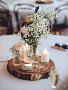 flowers and candles are placed in mason jars on a wood slice at a wedding reception