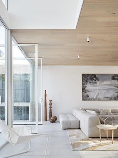 a modern living room with white furniture and wood ceilinging, along with large windows