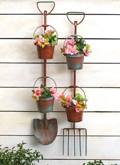 three pots with pink flowers are hanging on a wall next to a garden rake and flower pot holder