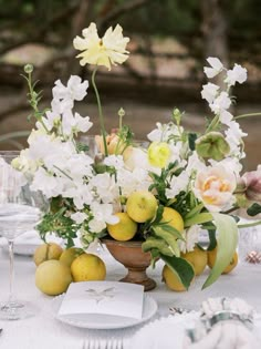 an arrangement of flowers and lemons on a table set for a formal dinner party