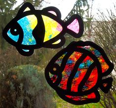 two stained glass fish sitting on top of a window sill in front of trees