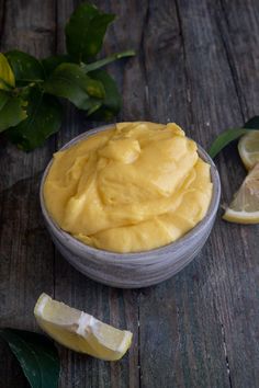 a wooden table topped with a small bowl filled with yellow liquid next to sliced lemons