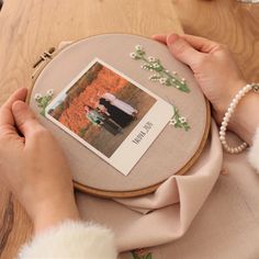 a woman is holding a photo in front of a cross stitch project