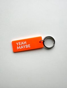 an orange keychain with the words yeah maybe printed on it, sitting on a white surface