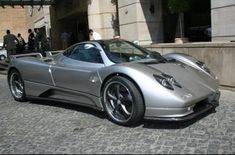 a silver sports car parked in front of a building with people standing around it on the sidewalk