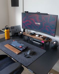 a computer desk with a keyboard, mouse and monitor on it in front of a large screen