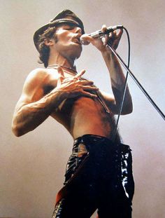 a man with no shirt on holding a microphone and singing into a mic in front of him