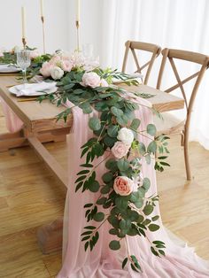 the table is set with pink flowers and greenery on it, along with candles