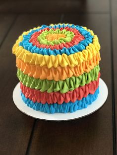 a multicolored cake with ruffles on top sits on a white plate