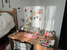 a wooden desk topped with a computer keyboard and mouse next to a bed covered in sheets