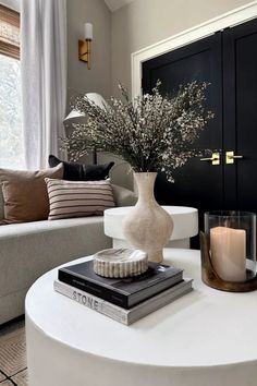 a white table topped with a vase filled with flowers next to a couch and window