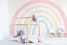 a child's room decorated in pastel colors with a rainbow painted wall behind it