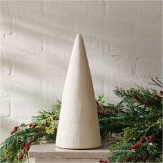 a white vase sitting on top of a table next to evergreen branches and red berries