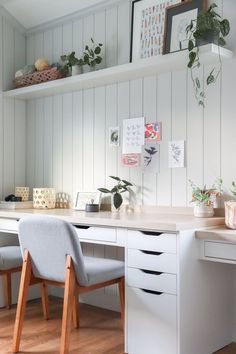 a white desk with two chairs next to it and some plants on the shelf above