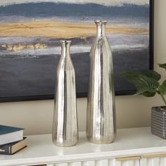 two silver vases sitting on top of a white table next to a book shelf