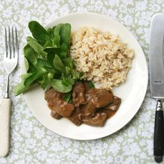 a white plate topped with meat, rice and spinach next to a knife and fork