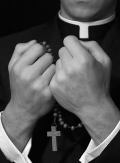 a man in a priest's outfit holding his hands together with the cross on it