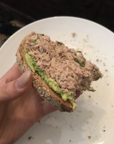 a hand holding a sandwich with tuna and avocado