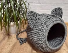 a crocheted cat bed is sitting on the floor next to a potted plant