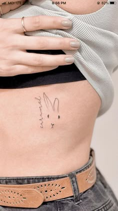 a woman's stomach with a rabbit tattoo on her belly and the word love written in cursive writing