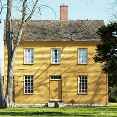 a large yellow house with two windows and a tree in front of it on a sunny day