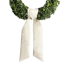 a white ribbon tied to a wreath with green leaves on the front and back side