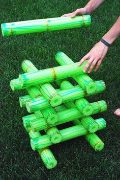 two hands reaching for a stack of green frisbees on the grass in front of each other