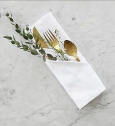 a fork, knife and spoon in a napkin on a marble counter top with greenery