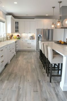 a large kitchen with white cabinets and wood flooring on the countertops, along with bar stools