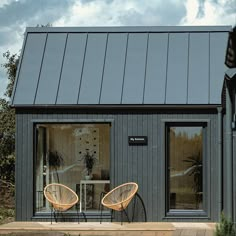 two wicker chairs sitting on top of a wooden deck next to a gray building