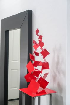 a red sculpture sitting in front of a mirror on top of a table next to a doorway