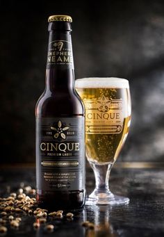 a bottle and glass filled with beer sitting on top of a table next to grains